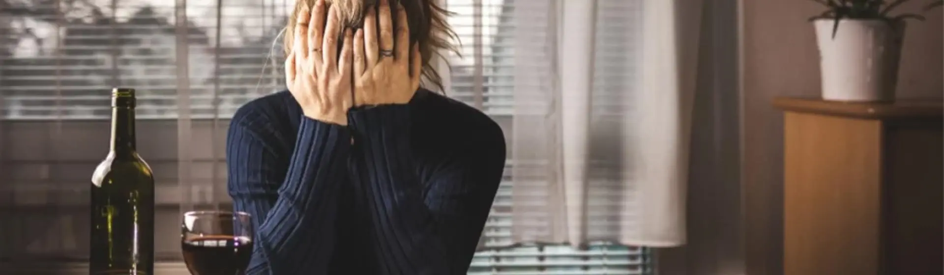 Frustrated woman sitting in front of a bottle and glass of wine.
